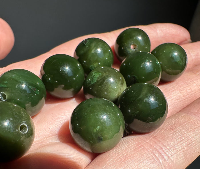 Polished dark green Cassiar jade beads held in a hand