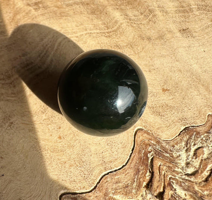 Single 16mm dark green Canadian nephrite jade bead on a beige textured surface