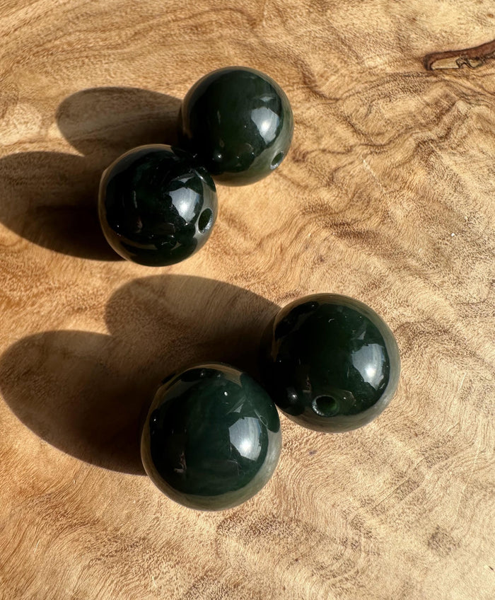 Three 16mm dark green Canadian nephrite jade beads with drilled holes on a brown textured surface