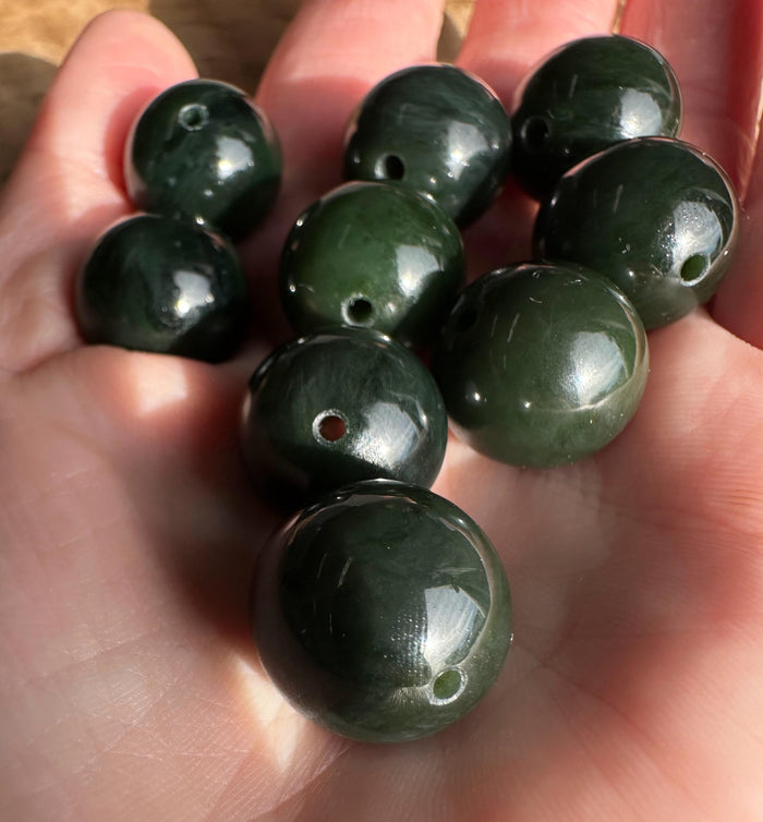 Several 16mm dark green Canadian nephrite jade beads with drilled holes held in a hand