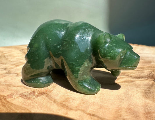 Small green stone bear walking sculpture on a wooden surface