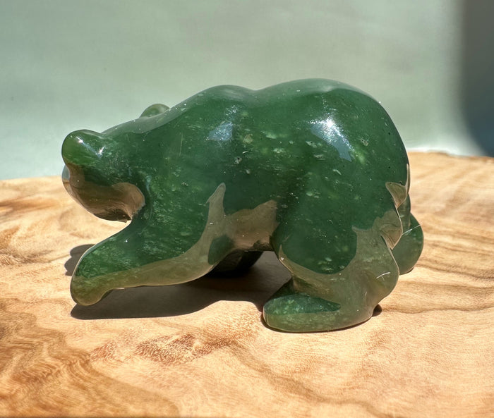 Green jade bear walking sculpture on a wooden surface