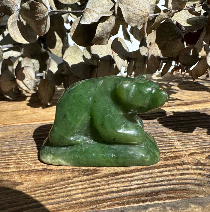 Small jade bear figurine on a wooden surface with dried beige leaves in the background