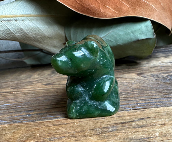 Side view of a glossy dark green jade bear sculpture on a wooden surface