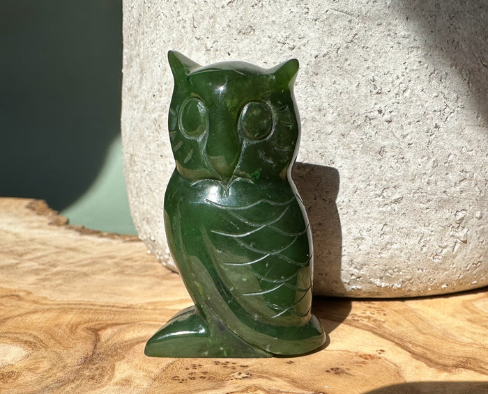 Two inch dark green jade owl figurine with a chipped edge resting on a wooden surface.