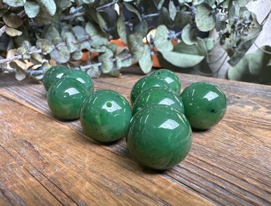 Group of polished 20mm green jade beads with drilled holes on a wooden surface