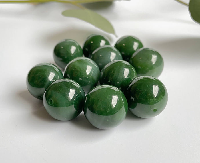 Polished green jade beads with drilled holes arranged in a cluster on a white surface