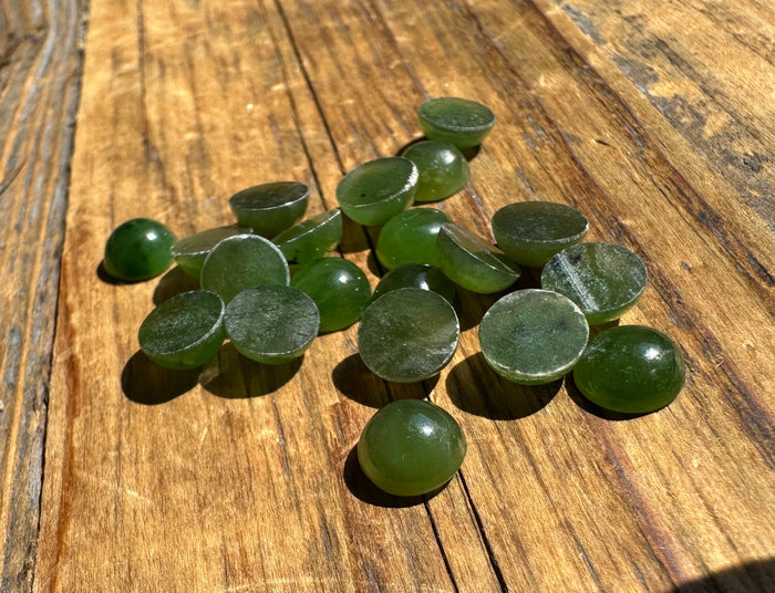 Group of 7mm round nephrite jade cabochons in green on a wooden surface