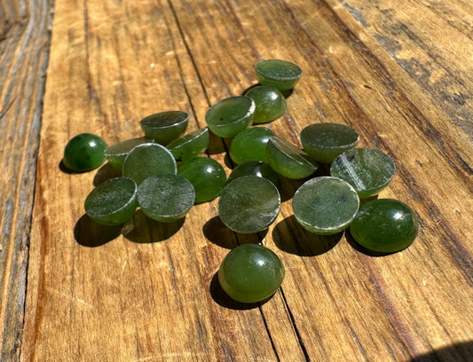 Group of 7mm round nephrite jade cabochons in green on a wooden surface