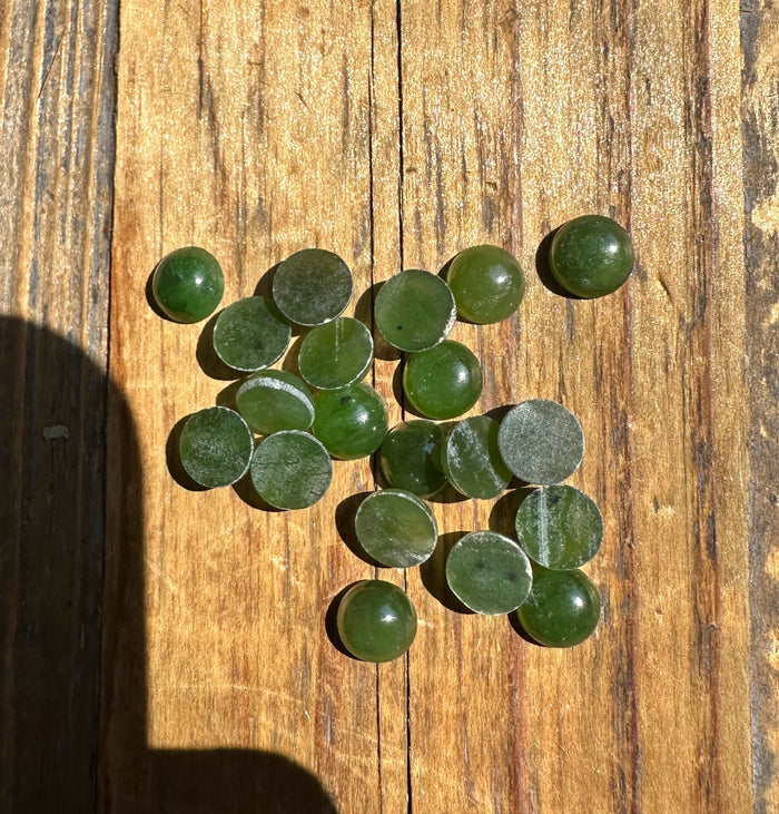 Twenty 7mm round nephrite jade cabochons scattered on a wooden surface.