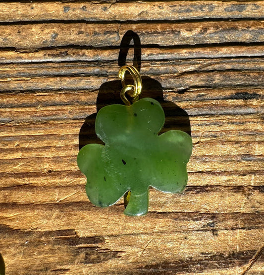 Green jade three leaf clover pendant with a gold bail on a wooden background