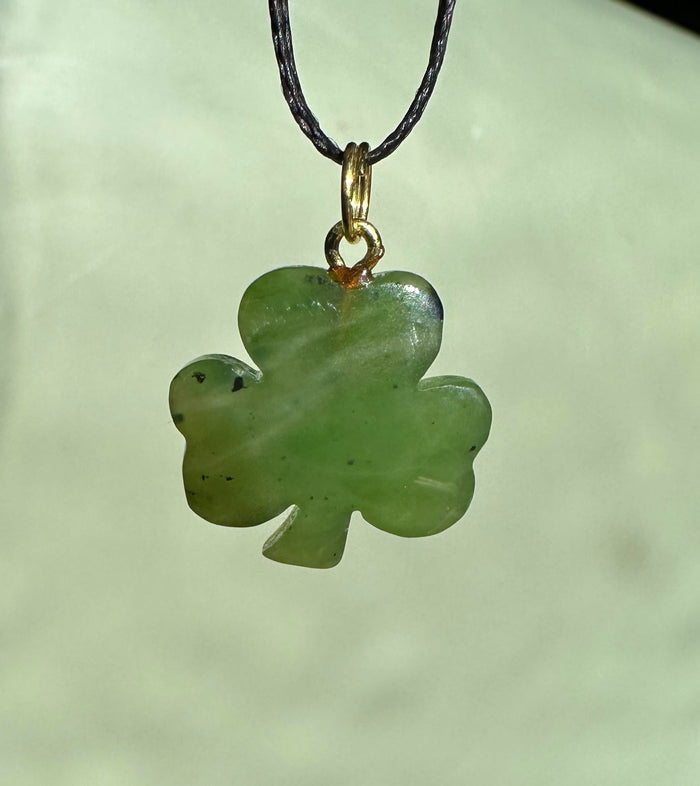 Close up of a green jade three leaf clover pendant hanging from a black cord with a gold bail