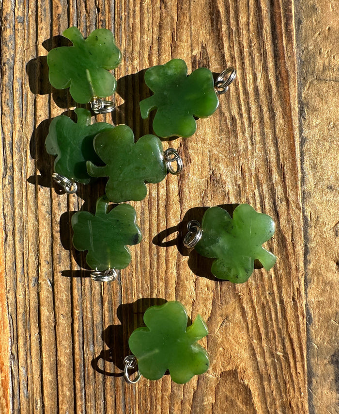 Group of green clover shaped pendants with silver loops displayed on a weathered wooden surface