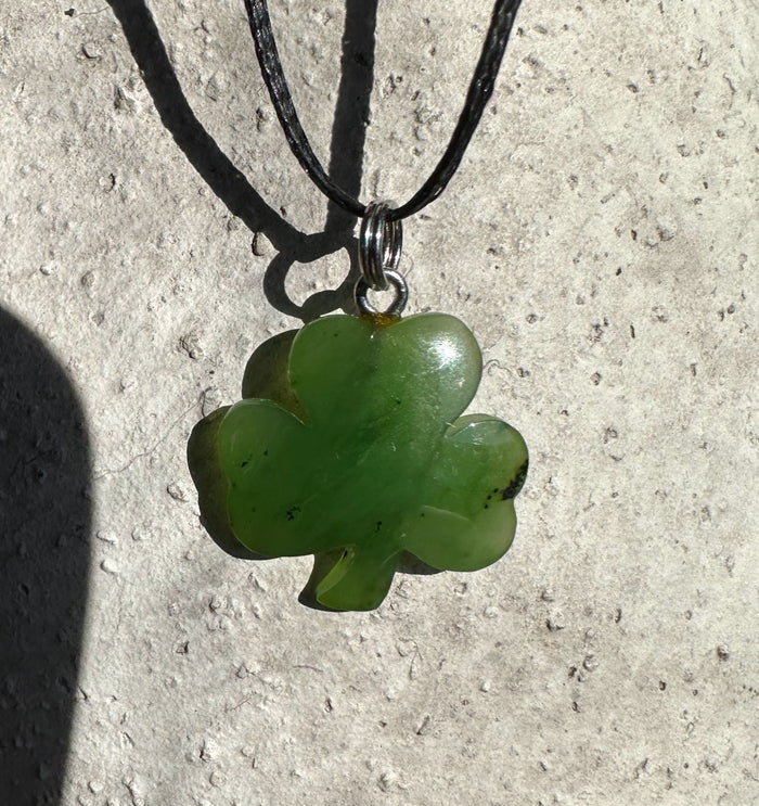 Green clover pendant on a black cord necklace with a metal bail against a light textured background