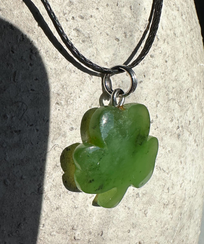 Close up of glossy green clover pendant with metal bail on a black cord necklace
