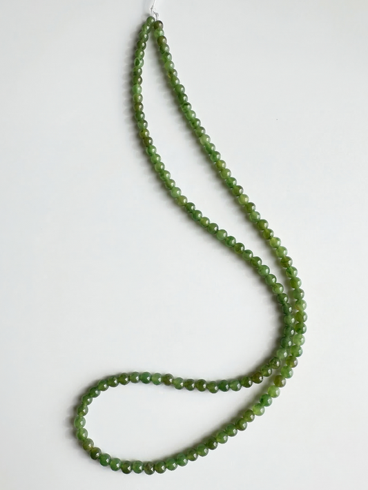 Green nephrite jade beads on white background formed into a long unstrung strand