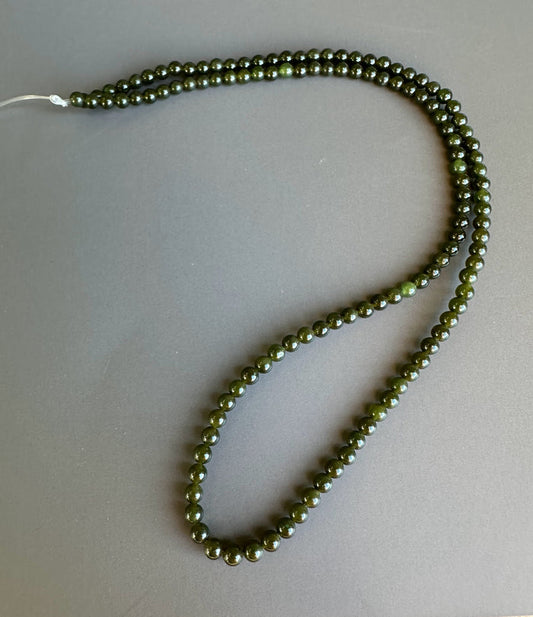 Dark green 3mm nephrite jade beads on an unstrung strand coiled against a gray backdrop.