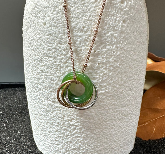 Green jade circle pendant with four interlocking rings on a rose gold chain