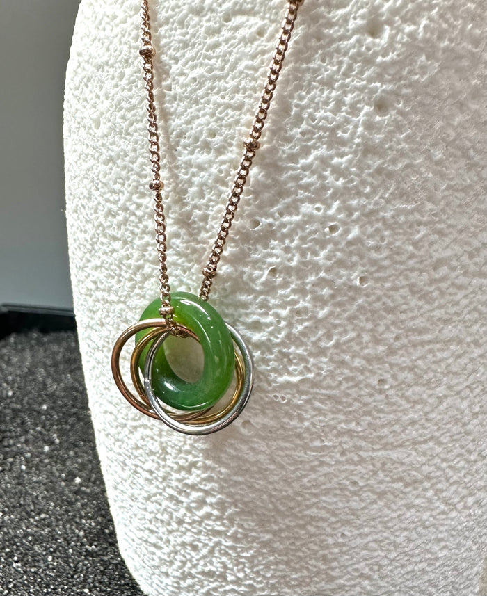 Four ring pendant necklace with a green jade donut and interlocking gold silver and bronze rings.