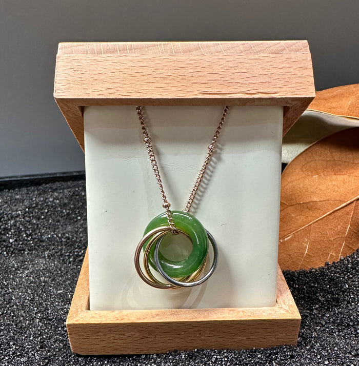 Pendant on a rose gold chain displayed in a wooden box with a green jade donut and interlocking rings.