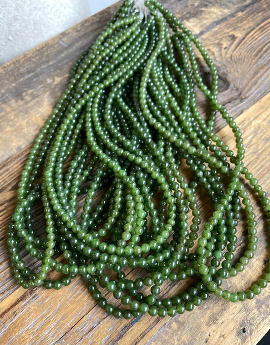 Several strands of 4mm nephrite jade beads in green hues on a wooden surface
