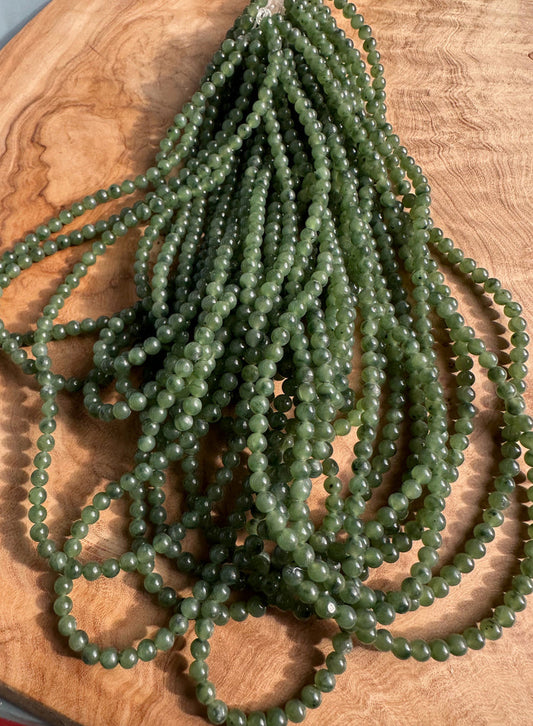 Numerous 4mm green nephrite jade beads arranged in strands on a wooden surface