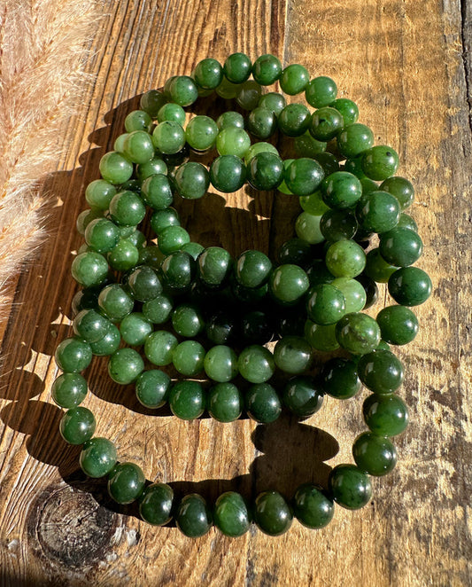 8mm green jade bead bracelet with elastic cord coiled on a wooden surface