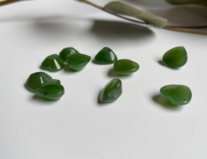 Small green jade heart cabochons sold individually scattered on white surface