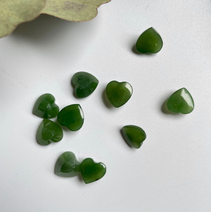 Group of green jade heart cabochons on a white background with a dried leaf in the corner