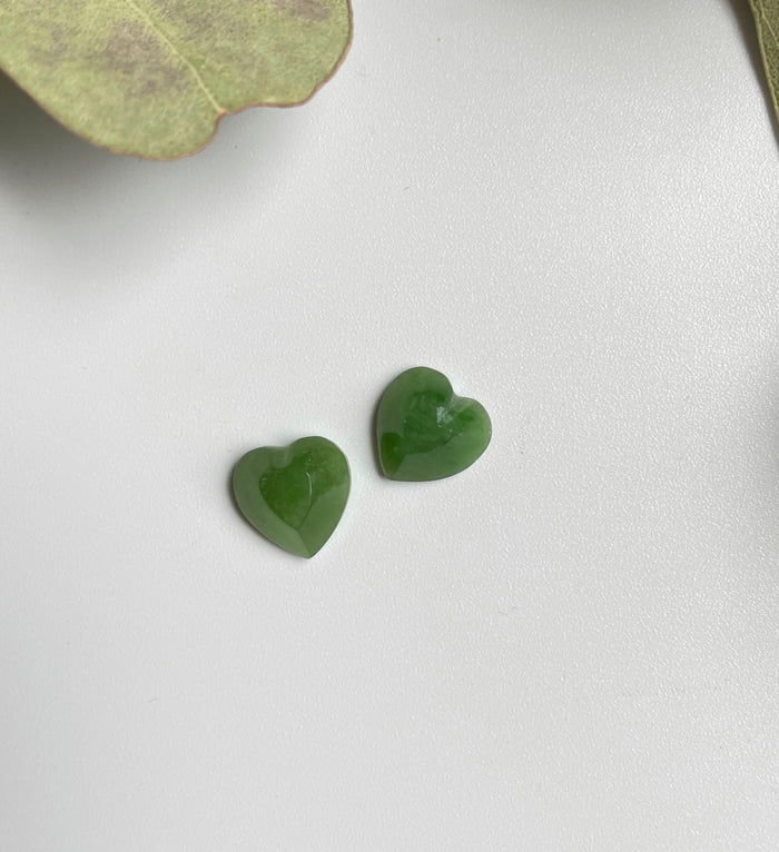 Two glossy green jade heart cabochons on a light background