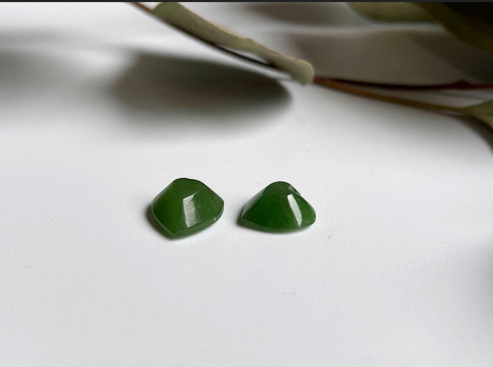 Two glossy green jade heart cabochons resting on a white surface
