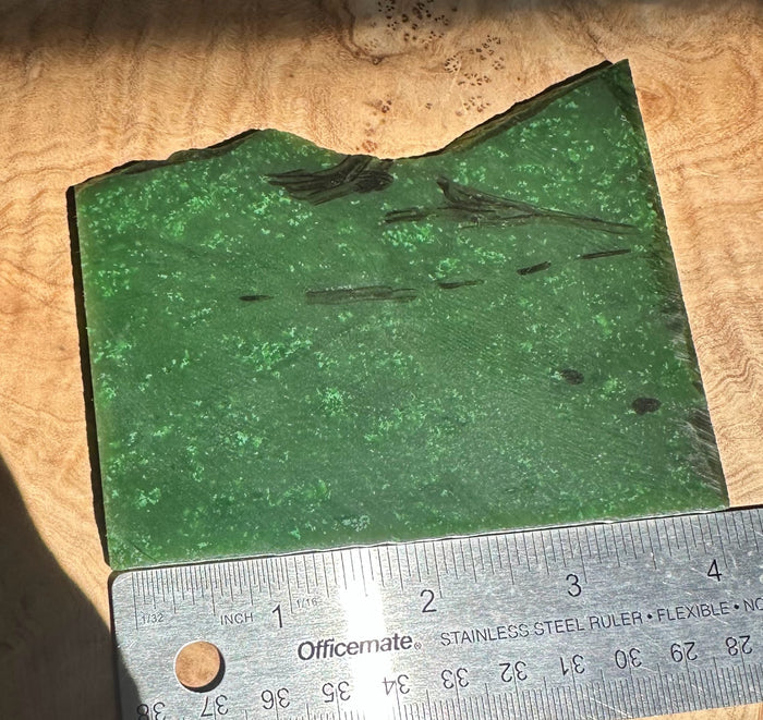 A Grade Cassiar jade slab in green on a wood surface with a ruler for scale
