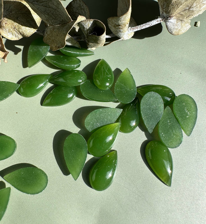 Bright green nephrite jade pear cabochons arranged on a light background.