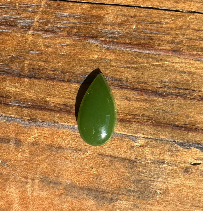 Single polished green nephrite jade pear cabochon on a wooden surface.
