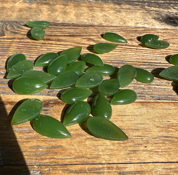 Group of green pear shaped jade cabochons on a rustic wooden surface