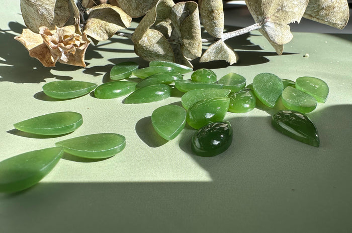 Assorted green nephrite jade pear cabochons scattered on a wooden surface