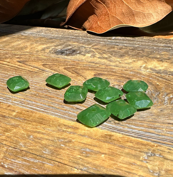 Green faceted Canadian jade beads 11.5x13.5 mm laid on a wooden surface