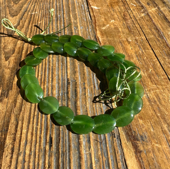 Two strands of green jade lentil beads tied with a cord bow on a wooden surface