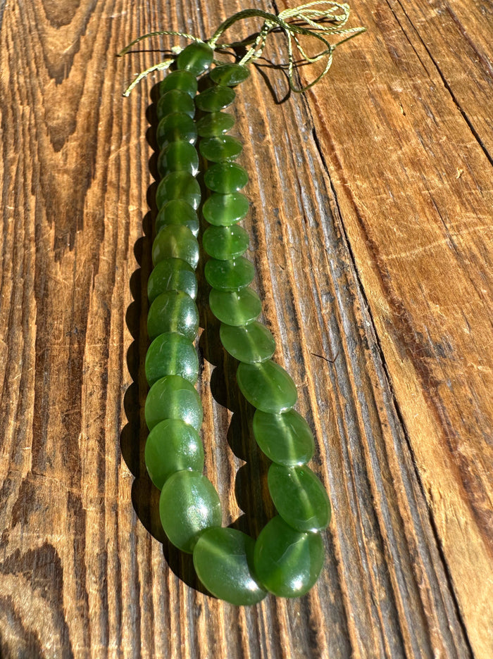 Single strand of green jade lentil beads laid on wood with a knotted cord at the end