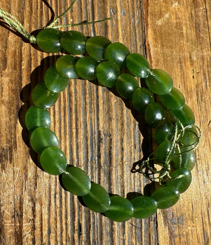 Long strand of green jade lentil beads on a weathered wooden surface.