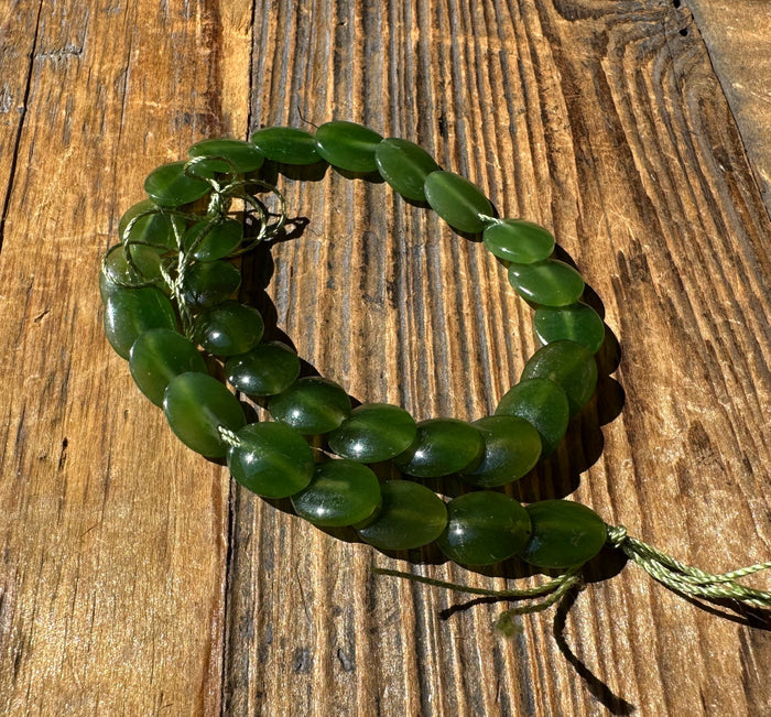 Spiral arrangement of green jade lentil beads on a wooden background.