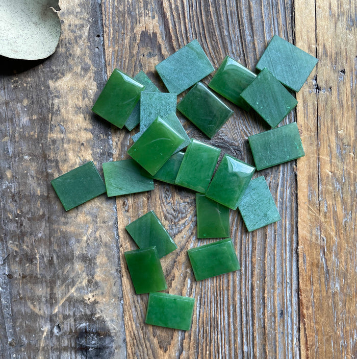 A grade emerald green rectangle cabochons 17.5x12.5mm scattered on a weathered wooden surface