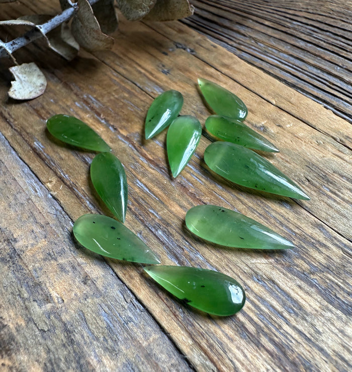 Loose green teardrop cabochons on a rustic wooden surface