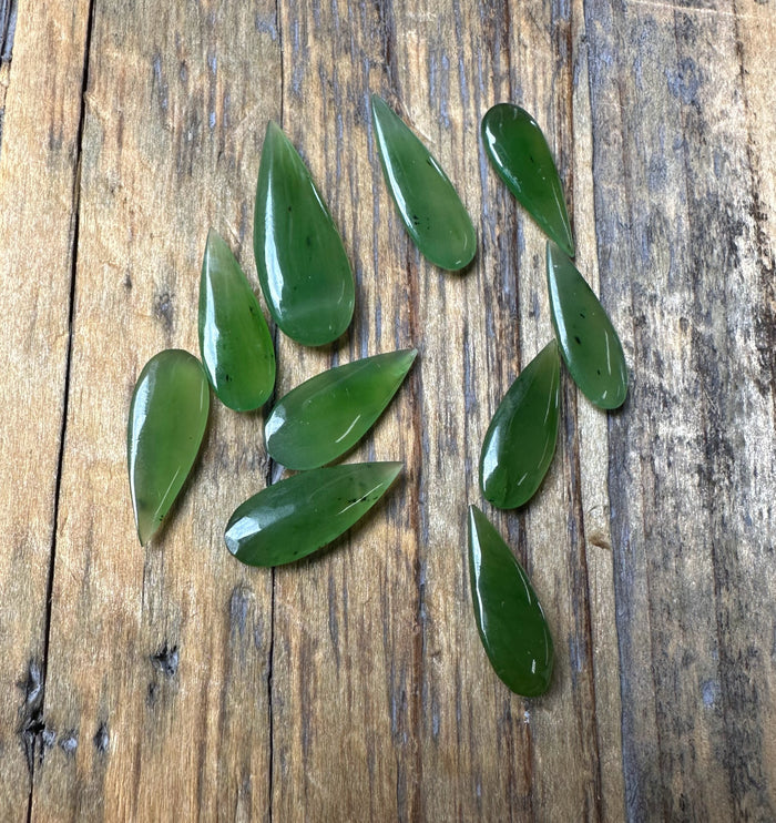 Several green teardrop cabochons scattered on a rustic wooden board