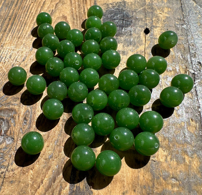 Glossy green jade beads spread across a wooden table, each with a visible stringing hole