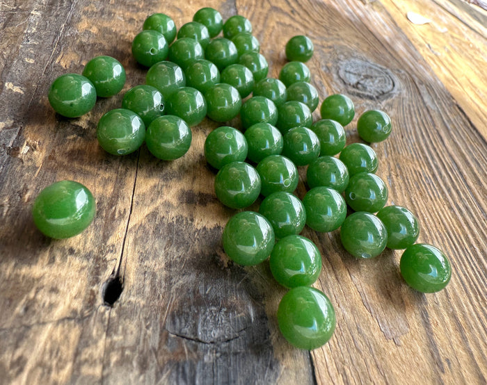 Close up of multiple green jade beads on wood showing round shapes and drill holes for stringing