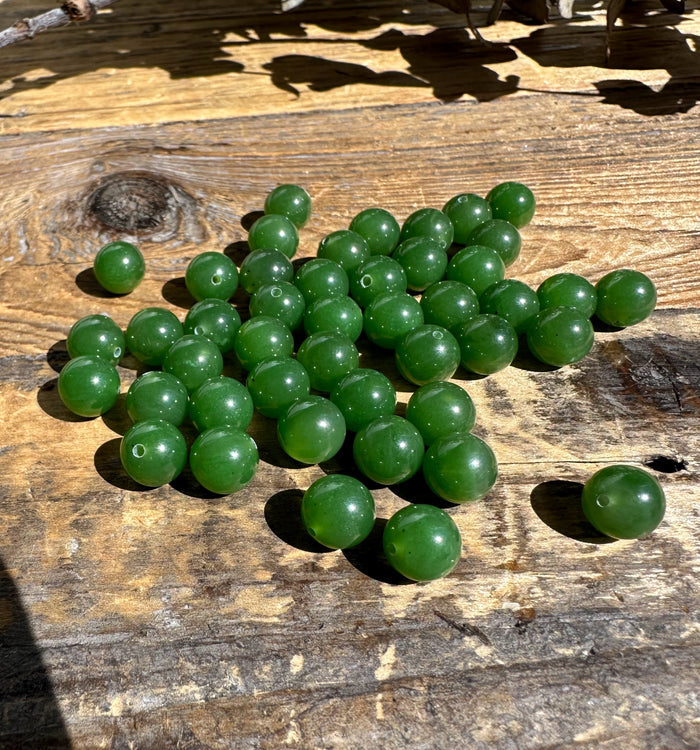 A+ half drilled 8mm Canadian jade beads scattered on a weathered wooden surface