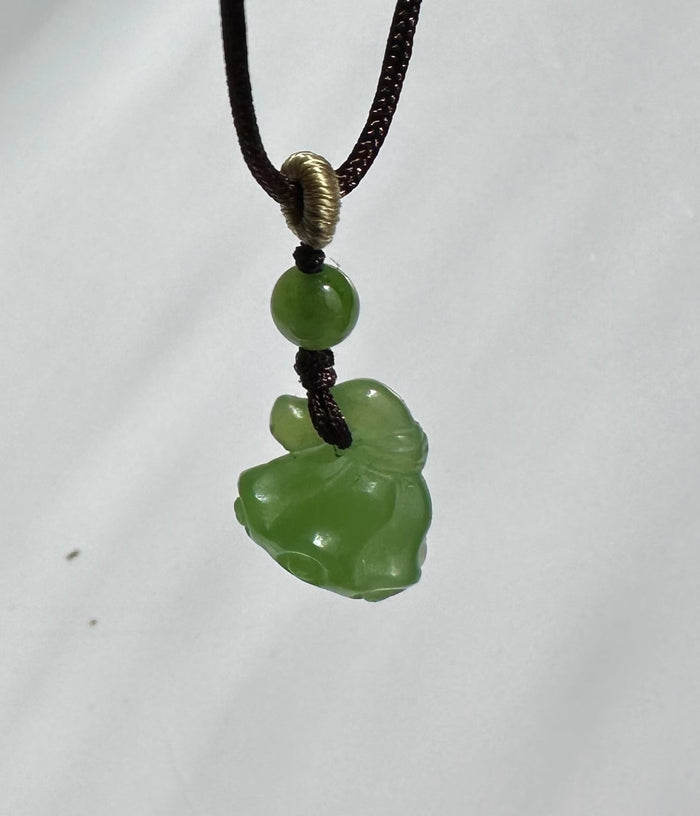 Green jade bead above a carved jade pendant on a brown cord with a wrapped loop
