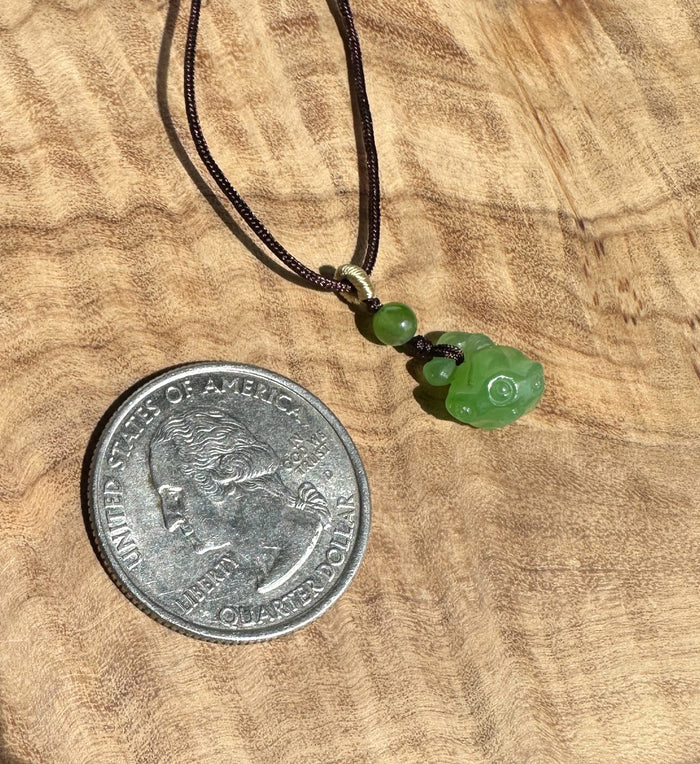 Green jade lotus seed pod pendant on a dark braided cord with a coin for scale