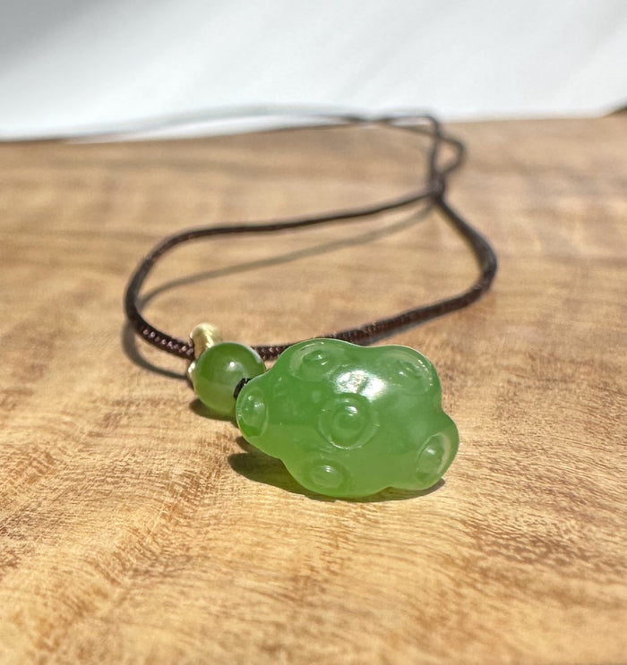 Close up of brown braided cord with a small green jade bead and knot near the pendant